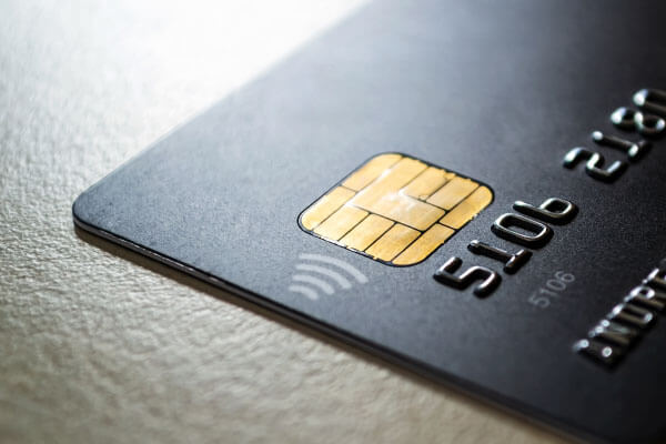 Black credit card with chip and contactless pay technology close-up. Low key shot with old credit card.